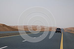 A car drives on an empty road in the deserts of Dubai, UAE