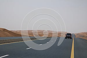 A car drives on an empty road in the deserts of Dubai, UAE