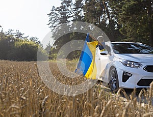 car drives off-road through a wheat field in summer. A boy with a Ukrainian yellow-blue flag