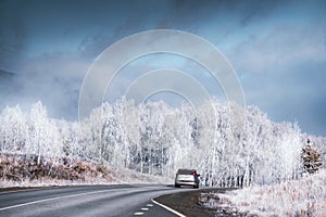 Car driving on asphalt road in winter mountains with frost-covered trees