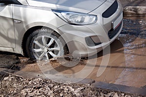 Car is driving through a big pothole filled with water. Dangerous destroyed roadbed.