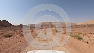 Car driving on a country road at the desert with mountains and blue sky in the background.