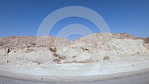 Car driving on a country road at the desert with mountains and blue sky in the background.