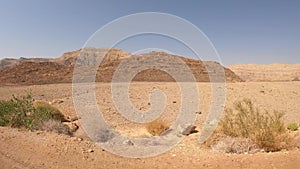 Car driving on a country road at the desert with mountains and blue sky in the background.