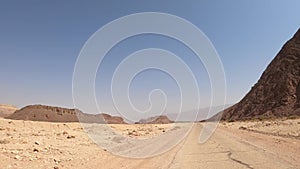 Car driving on a country road at the desert with mountains and blue sky in the background.