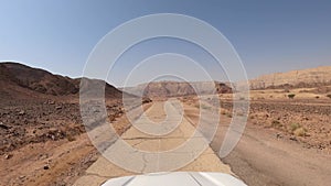 Car driving on a country road at the desert with mountains and blue sky in the background.