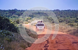 The car is driving on a dirt road in Tsavo National Park East Kenya. People are on a safari trip in nature.