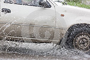 Car driving on a flooded road with water and splashes caused by heavy rain.