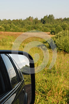 Car driving through the forest on a sunny road in the woods viewed from outside driver window with sky pouring through trees on an