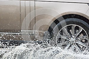 Car driving through a puddle on a flooded road with water and splashes caused by heavy rain.