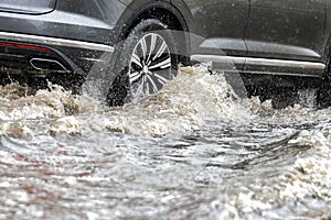 The car is driving through a puddle in heavy rain. Splashes of water from under the wheels of a car. Flooding and high water in