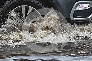 The car is driving through a puddle in heavy rain. Splashes of water from under the wheels of a car. Flooding and high water in