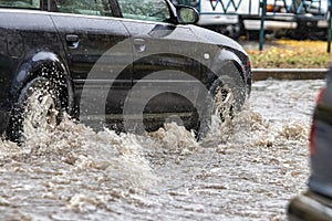 The car is driving through a puddle in heavy rain. Splashes of water from under the wheels of a car. Flooding and high water in