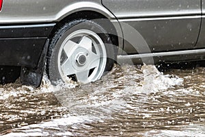 The car is driving through a puddle in heavy rain. Splashes of water from under the wheels of a car. Flooding and high water in