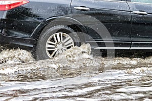 The car is driving through a puddle in heavy rain. Splashes of water from under the wheels of a car. Flooding and high water in