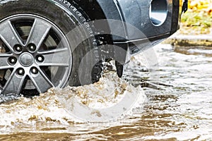 The car is driving through a puddle in heavy rain. Splashes of water from under the wheels of a car. Flooding and high water in