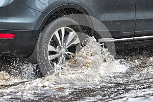 The car is driving through a puddle in heavy rain. Splashes of water from under the wheels of a car. Flooding and high water in