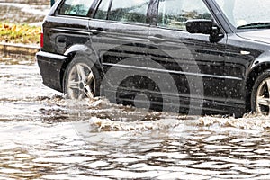 The car is driving through a puddle in heavy rain. Splashes of water from under the wheels of a car. Flooding and high water in