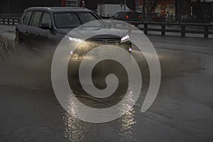 The car is driving in a puddle. Sprays from under the wheels