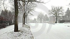 Car driving in a residential area during winter.  Wind blowing and snow fall