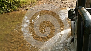 Car driving through shallow creek. View of car crossing shallow river while driving down remote road in forest of