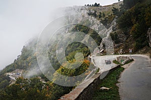 A car driving on a winding mountain road where white fog descends