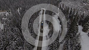 Car driving on winter country road in snowy forest, aerial view from drone