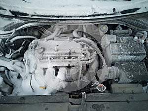 Car engine close-up. The engine compartment is covered with snow and ice after a long parking