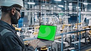 Car Factory Engineer in Work Uniform Using Laptop Computer with Green Screen Mockup Display. Working