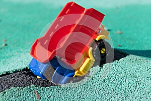 The car fell into the pit. Toy plastic truck with a red body had an accident. Hole on Asphalt Coating. The road needs