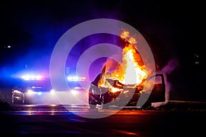 Car on fire at night with police lights in background