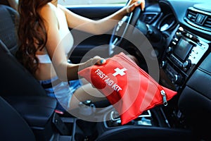 Car First Aid Kit in female hands on a steering wheel background.