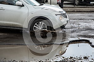 The car goes without reducing speed on a bad road with asphalt in pits and potholes, hitting the wheel in a puddle, spraying melt