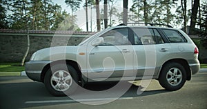 The car goes in a residential area of the city. gray SUV. the car rides on the road side view.