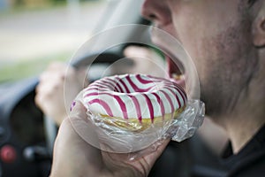 In the car, a hand to give a delicious doughnut to a man with an open mouth.