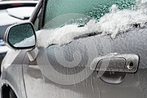 Car handle, mirror and window are covered with ice after freezing rain.