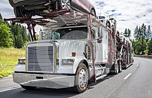 Car hauler white big rig classic semi truck transporting cars on the modular two level semi trailer running on the turning summer