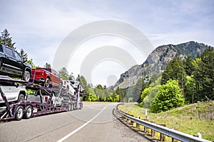 Car hauler white big rig semi truck transporting trucks on the two level hydraulic semi trailer driving on the highway road in