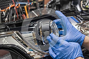 Car headlight in repair close-up. An auto mechanic wearing gloves installs the lens into the headlight housing.