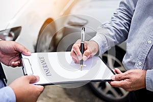 Car insurance agent send a pen to his customers sign the insurance form on clipboard while examining car after accident claim