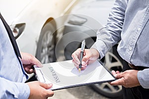 Car insurance agent send a pen to his customers sign the insurance form on clipboard while examining car after accident claim