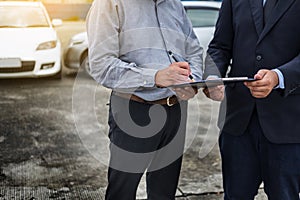 Car insurance agent send a pen to his customers sign the insurance form on clipboard while examining car after accident claim