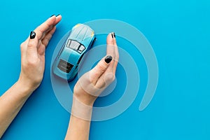 Car insurance concept. Safety of auto. Car toy in female hands on blue background top view copy space