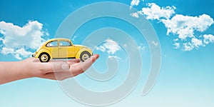 Car insurance concept with yellow car in hand. Clouds in background