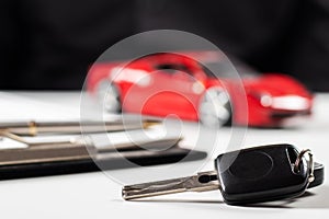Car insurance form, pen and key on wooden table, and red car background