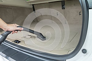 Car interior detailing vacuuming dust from a car carpet in the boot trunk