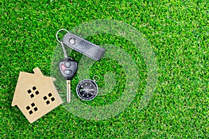 A car key and compass with small wooden toy house on green grass.