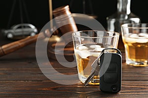 Car key, glass of alcohol near gavel on wooden table, space for text. Dangerous drinking and driving