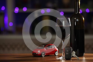 Car key, glass of alcohol near toy auto on wooden table against blurred lights, space for text. Dangerous drinking and driving