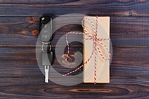 Car key near paper box with red ribbon bow on wooden table background. Christmas or Valentine`s Day gift or present abstract conc